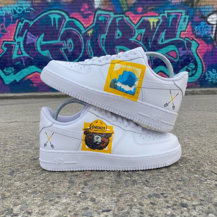 Custom Air Force 1 Blue Yellow Brown Cartoon Bear White sneakers with colorful patches on a concrete surface with graffiti in the background